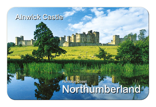 A rectangular souvenir-style print or card with rounded corners showing a landscape scene of Alnwick Castle in Northumberland, England. The artwork includes blue sky, white clouds, green grass and trees, and reflective water.